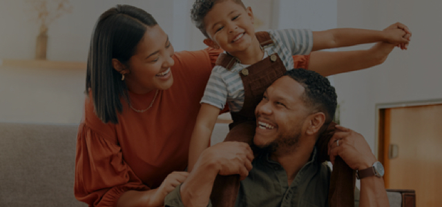 Parents and a young son laughing while the son is on the father's shoulders