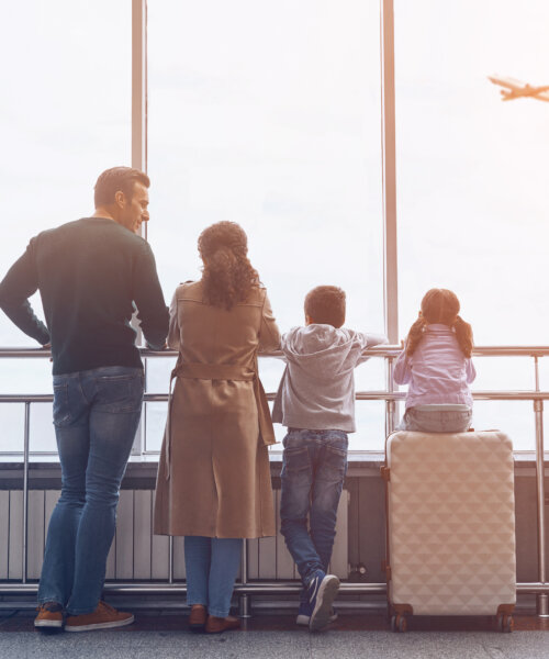 Full length of family with two little kids looking at the flying airplane while standing in airport terminal