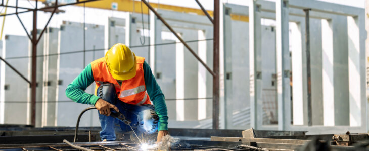 Workers at a construction site weld metal structures of precast concrete slabs.