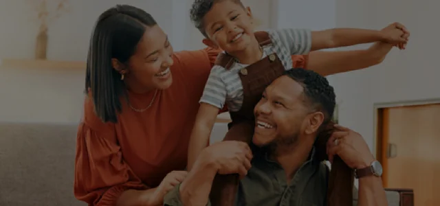 Parents and a young son laughing while the son is on the father's shoulders