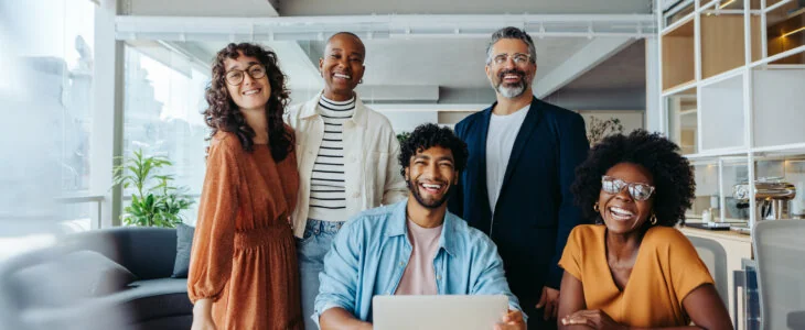 Successful business team working together in an office. They are happy, smiling and looking at the camera, representing their thriving startup company.